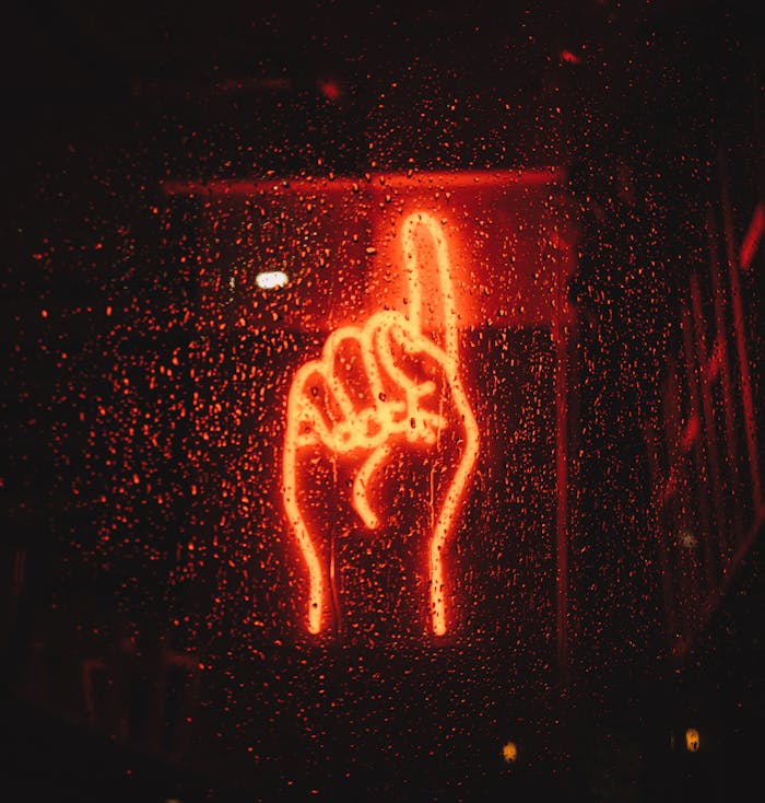 A vibrant neon hand sign seen through a wet window, creating a dramatic urban night scene.