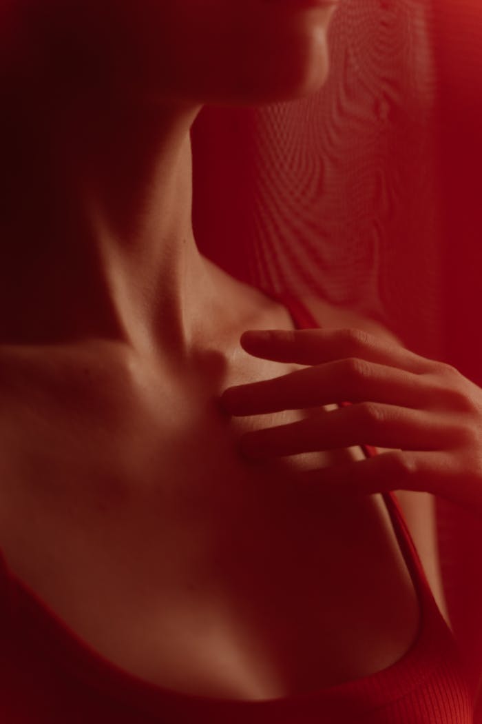 brand-02 Close-up of a person touching their chest with hands in soft red lighting, evoking intimacy.