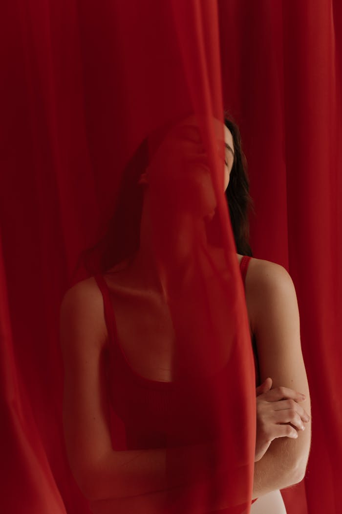 Elegant portrait of a woman partially concealed by a red sheer curtain, creating an enigmatic atmosphere.